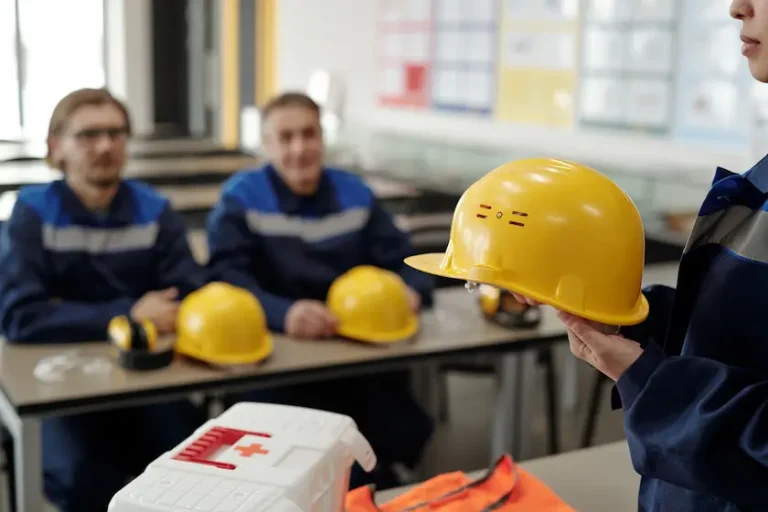 giovane-lavoratrice-uniforme-che-tiene-il-casco-protettivo-mentre-si-trova-di-fronte-colleghi-maschi-alla-lezione-di-basi-della-sicurezza-della-vita